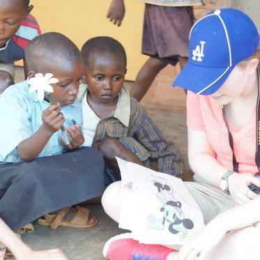 一位戴着蓝色棒球帽的妇女给坐在她周围感兴趣的孩子们读书. 一个拿着一朵花.