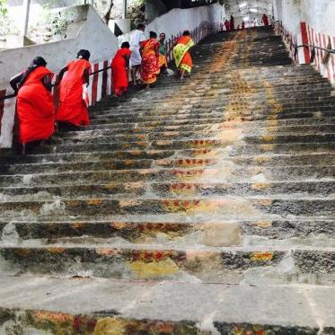 穿着鲜橙色衣服的人们走上一段长长的旧石阶楼梯，来到一座寺庙.